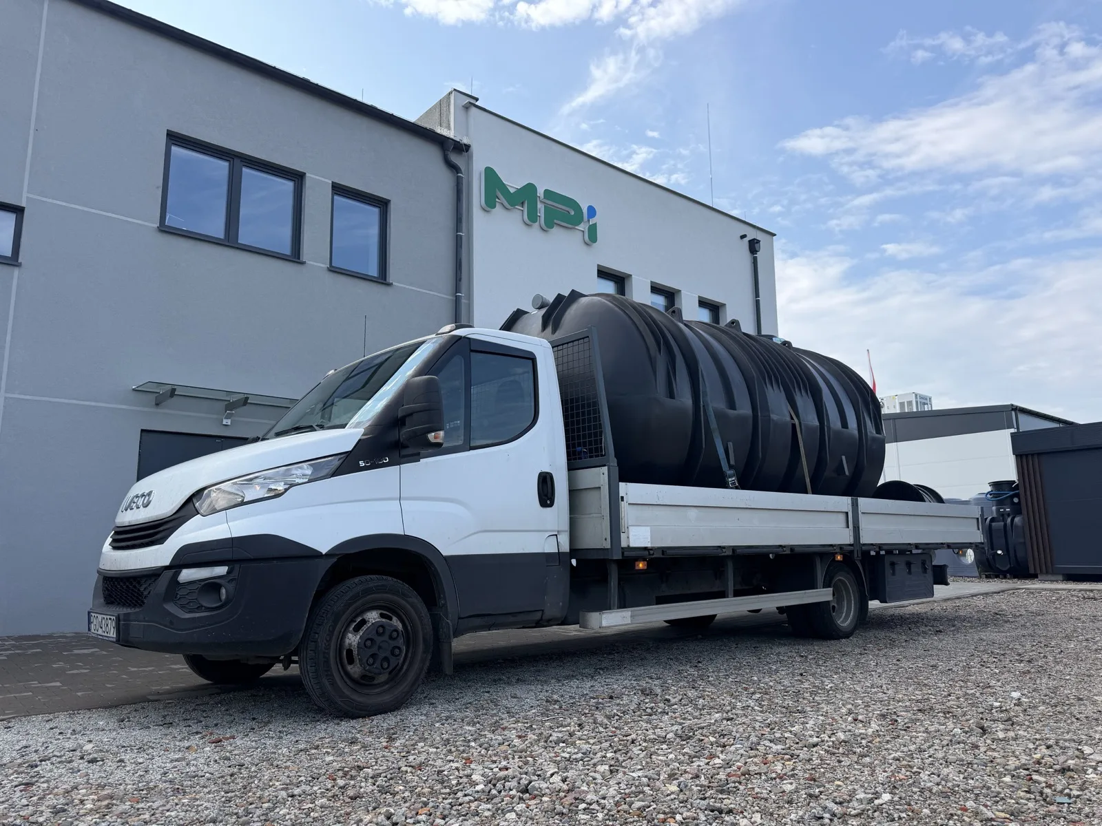 Zbiornik retencyjny MPI EcoLine II załadowany na ciężarówkę IVECO przed budynkiem producenta z logo MPI — dostawa na budowę